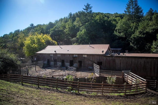 rear view of property featuring a wooded view, metal roof, an exterior structure, and an outdoor structure