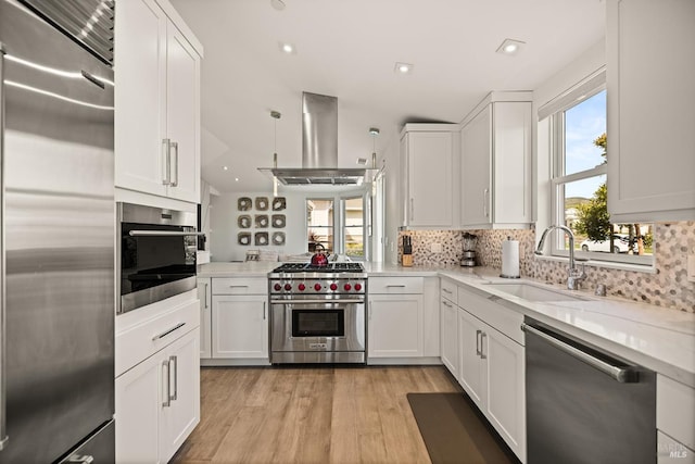 kitchen with high quality appliances, a sink, tasteful backsplash, white cabinets, and island range hood