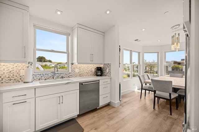 kitchen featuring light wood finished floors, a sink, white cabinets, dishwasher, and backsplash