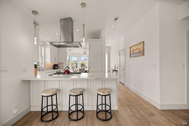 kitchen with visible vents, a peninsula, decorative backsplash, light countertops, and island range hood