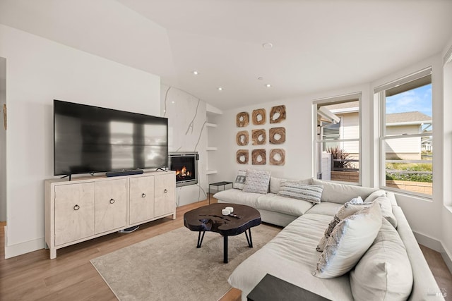 living room featuring recessed lighting, baseboards, light wood-style flooring, and a high end fireplace