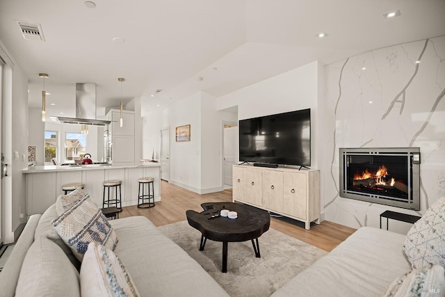 living room with a high end fireplace, visible vents, recessed lighting, and light wood-type flooring