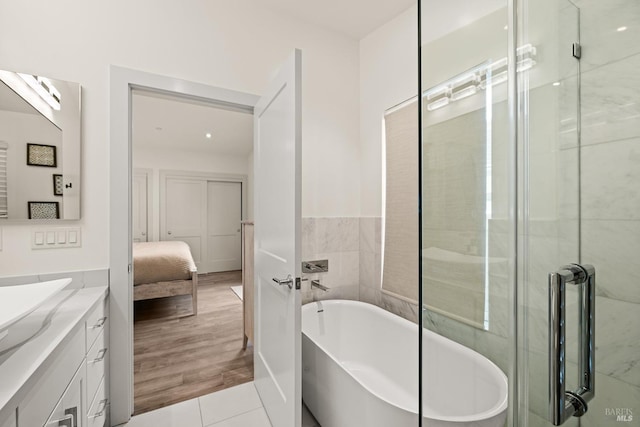 full bath featuring vanity, a soaking tub, and tile walls