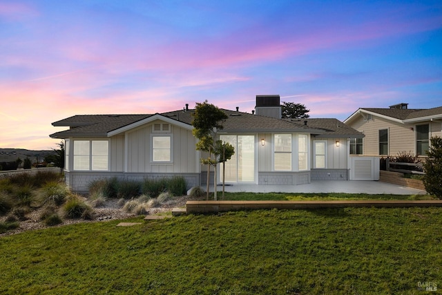 back of house at dusk featuring a yard, a patio area, and board and batten siding