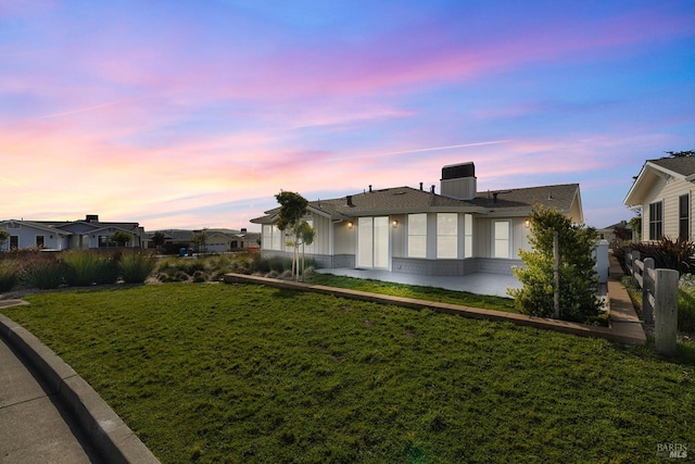 back of house at dusk with a yard and a patio