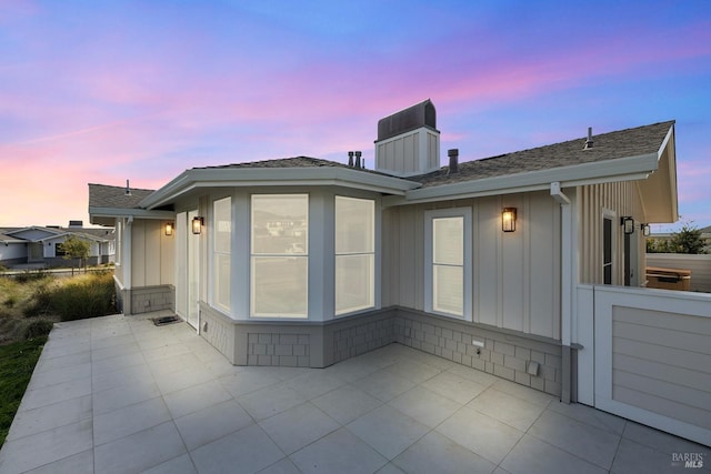 rear view of house featuring a patio, board and batten siding, and roof with shingles