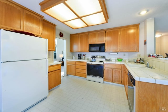 kitchen with black appliances, light floors, a sink, and tile counters