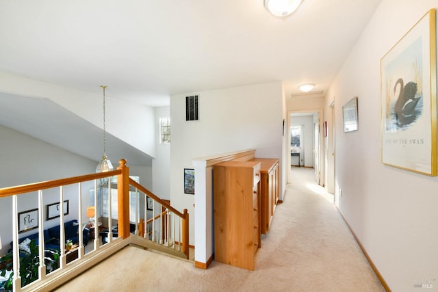 hallway with baseboards, visible vents, light colored carpet, and an upstairs landing