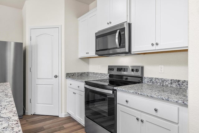 kitchen featuring white cabinets, light stone countertops, wood finished floors, and appliances with stainless steel finishes