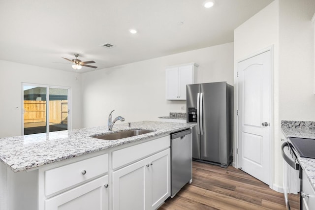 kitchen with a kitchen island with sink, a sink, wood finished floors, white cabinetry, and appliances with stainless steel finishes