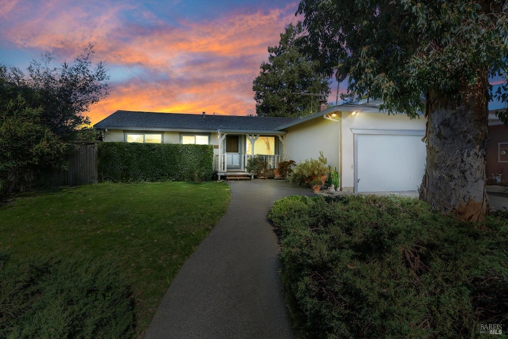 ranch-style house featuring an attached garage, fence, driveway, stucco siding, and a front yard