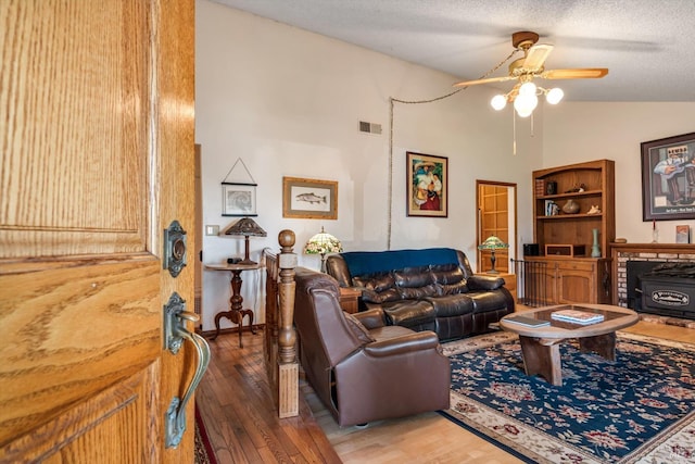 living room with a wood stove, visible vents, vaulted ceiling, and hardwood / wood-style flooring