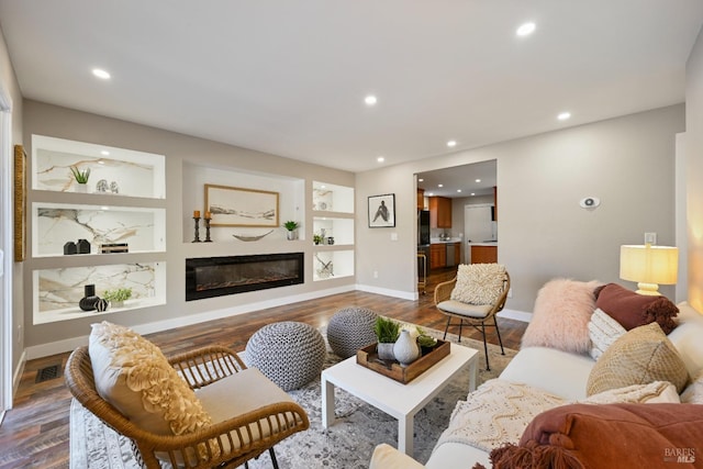 living area with built in features, dark wood finished floors, baseboards, a glass covered fireplace, and recessed lighting