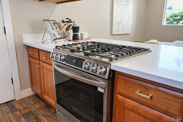 kitchen with stainless steel gas range, dark wood-style flooring, brown cabinetry, and light countertops