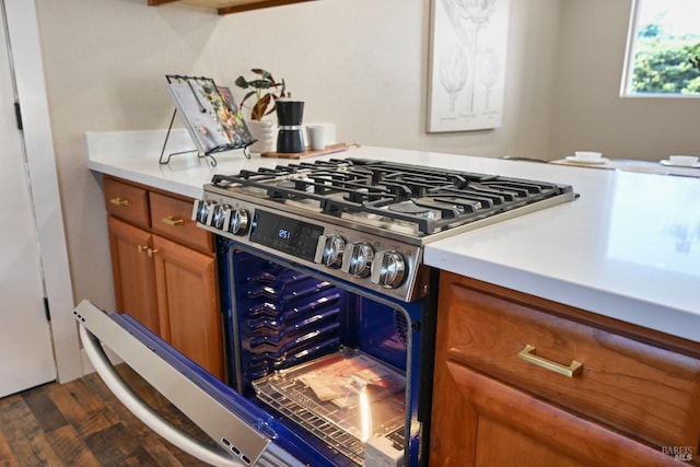 kitchen with stainless steel gas range oven, dark wood-style flooring, brown cabinetry, and light countertops