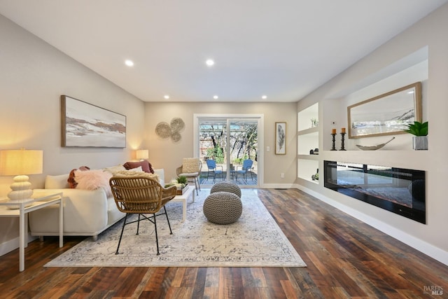 living room with built in shelves, recessed lighting, wood finished floors, baseboards, and a glass covered fireplace