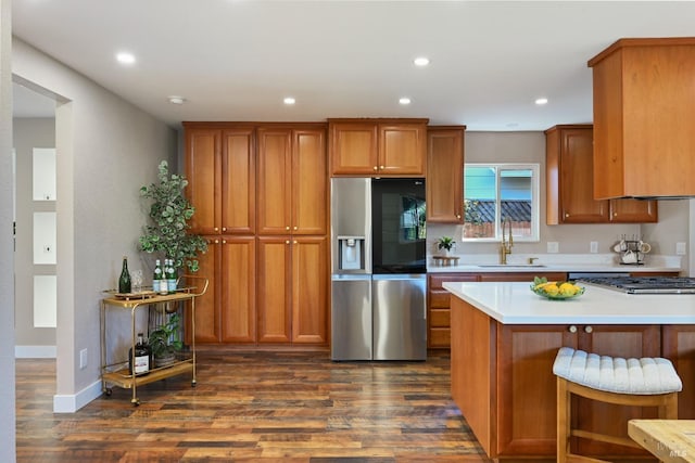 kitchen with a sink, gas stovetop, stainless steel refrigerator with ice dispenser, brown cabinets, and dark wood-style floors