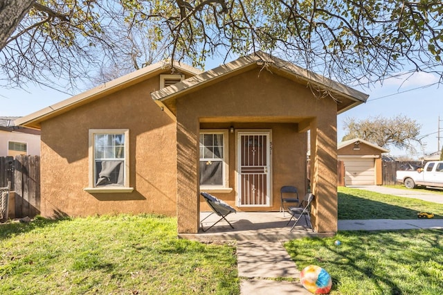 view of front of home featuring concrete driveway, an outbuilding, fence, a front yard, and stucco siding