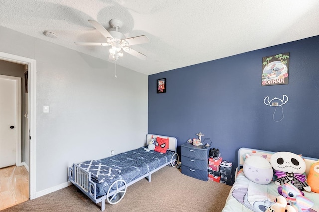 carpeted bedroom with a textured ceiling, ceiling fan, and baseboards