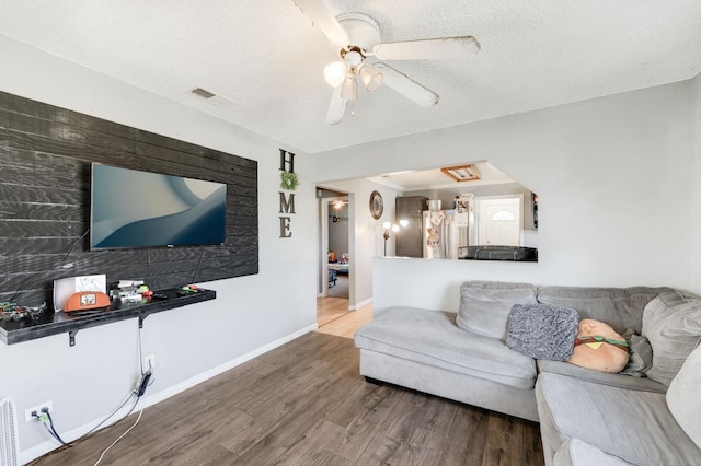 living room with a textured ceiling, ceiling fan, wood finished floors, visible vents, and baseboards