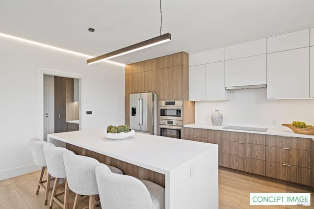 kitchen with light wood-type flooring, a kitchen island, appliances with stainless steel finishes, and a kitchen breakfast bar