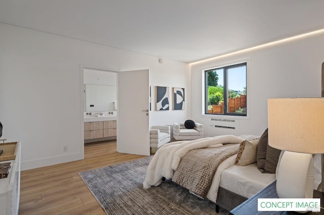 bedroom featuring a wall mounted air conditioner, ensuite bath, light wood-style flooring, and baseboards