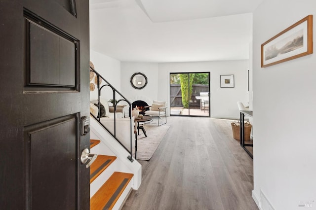 foyer entrance with a warm lit fireplace, stairway, and wood finished floors