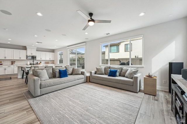 living room with visible vents, baseboards, a ceiling fan, light wood-style flooring, and recessed lighting