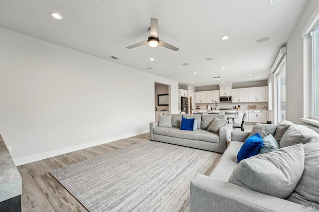 living room with light wood-style flooring, recessed lighting, visible vents, and baseboards