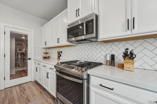 kitchen featuring stainless steel appliances, tasteful backsplash, light wood-type flooring, and white cabinetry