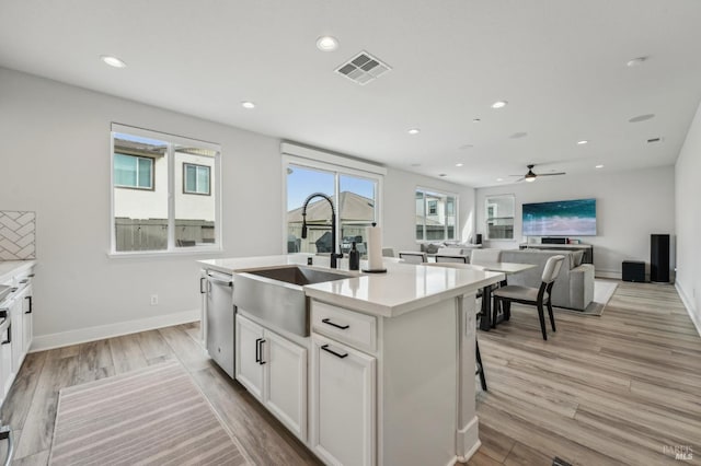 kitchen featuring a center island with sink, visible vents, light wood-type flooring, white cabinetry, and a sink