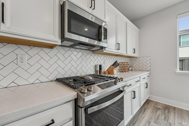 kitchen with light wood finished floors, stainless steel appliances, tasteful backsplash, white cabinetry, and baseboards