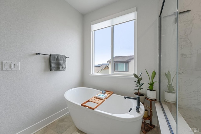 bathroom featuring a freestanding bath, a textured wall, a marble finish shower, and baseboards