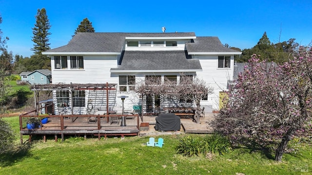 rear view of house featuring roof with shingles, a lawn, a deck, and a pergola