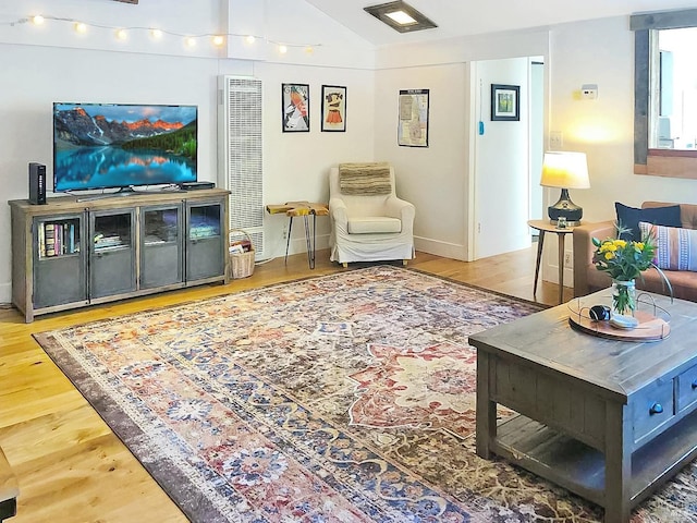 living area featuring lofted ceiling, baseboards, and wood finished floors