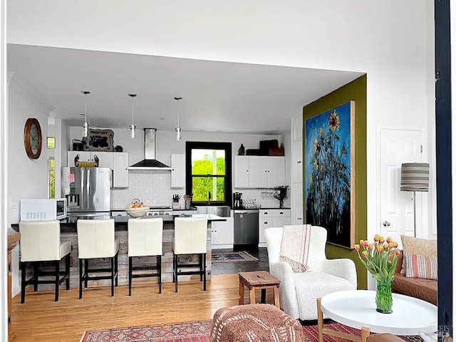 kitchen featuring light wood-style flooring, a breakfast bar, stainless steel appliances, wall chimney range hood, and white cabinetry