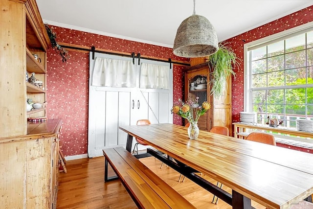 dining space with a barn door, wood finished floors, baseboards, wallpapered walls, and crown molding