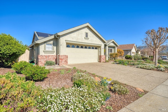 view of front facade with an attached garage, solar panels, brick siding, driveway, and stucco siding