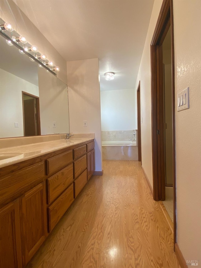 bathroom with double vanity, a garden tub, a sink, and wood finished floors