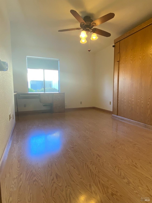 empty room featuring wood finished floors, a ceiling fan, and baseboards