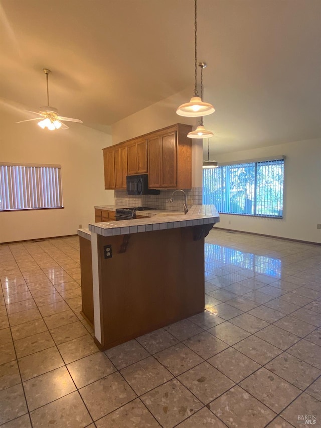 kitchen featuring decorative backsplash, a ceiling fan, tile countertops, a peninsula, and black microwave