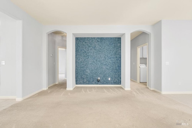 empty room featuring washer / dryer, an accent wall, arched walkways, and light colored carpet