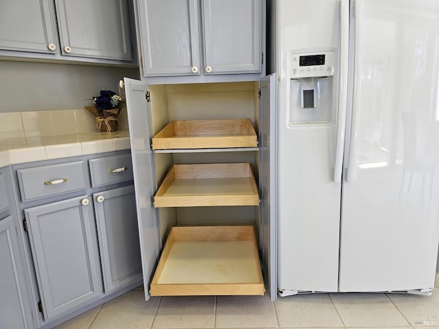 interior space featuring gray cabinetry, white refrigerator with ice dispenser, tile counters, and light tile patterned flooring