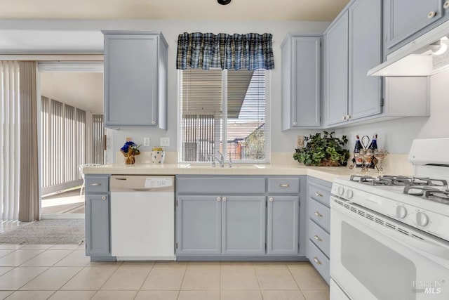 kitchen featuring white appliances, gray cabinets, under cabinet range hood, a sink, and light tile patterned flooring