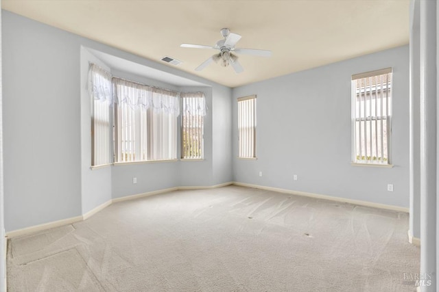 carpeted spare room with baseboards, visible vents, and ceiling fan