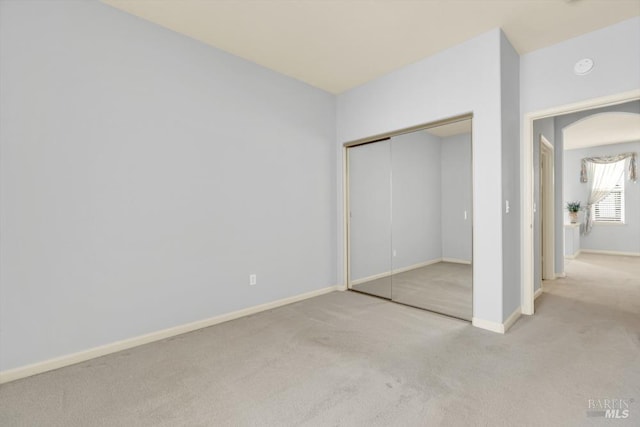 unfurnished bedroom with carpet, a closet, arched walkways, and baseboards