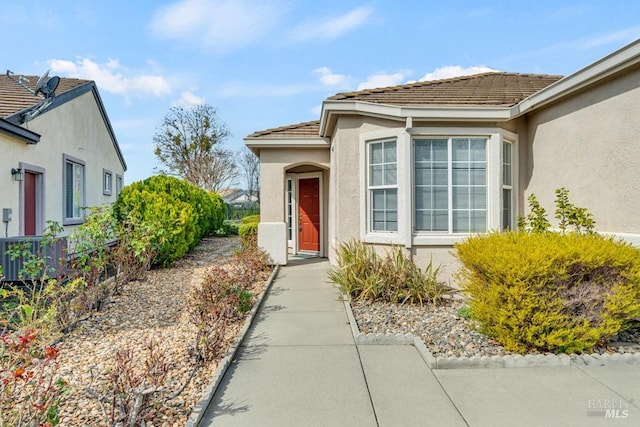 view of exterior entry featuring a tile roof, cooling unit, and stucco siding