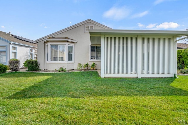 back of property featuring a lawn and stucco siding