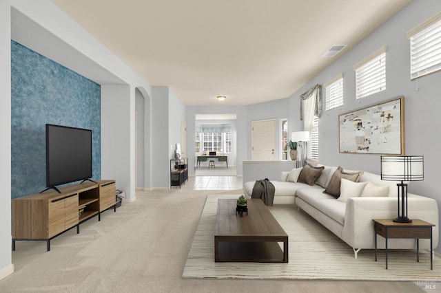 living area with arched walkways, a wealth of natural light, carpet flooring, and visible vents