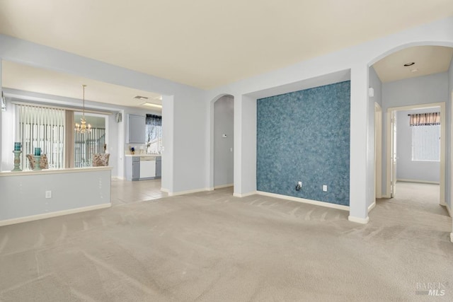 empty room featuring light carpet, an accent wall, arched walkways, and baseboards